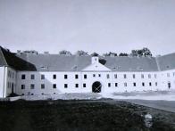 Snímek je datován. Je u něj záznam, že byl fotografován 28. října 1943. Autorem snímku je oficiální fotograf tehdejšího STW (Sudetenländische Treibstoffwerke AG), tedy chemických závodů.

Výstavba Osady, v době jejího vzniku v období II. světové války, kdy Němci budovali bydlení pro zaměstnance nedalekého chemického komplexu v Záluží, původně nazývaná Kaulangen, a později, kdy už byla část čtvrti realizována, byla nazvána Siedlung - sídliště, osada.

Těžiště výstavby spočívalo v založení nové městské čtvrti Litvínova, tehdy Oberleutensdorf, tzv. na zelené louce. Z hlediska stavebního vývoje Litvínova se jedná o vynikající urbanistické dílo.

Zajímavostí našeho obrázku je skutečnost, že nad průchodem směrem k Loutkárně, je původně věžička s hodinami, kterou bychom tam dnes už marně hledali. V knize Litvínov v proměnách času, vydané v roce 2003, se také objevuje pohled do ulice S. K. Neumanna z roku 1961, kde už je prostor nad podloubím v podobě, v jaké jej známe dnes. Kdy a za jakých okolností věžička z průčelí zmizela, nám zatím není známo.


